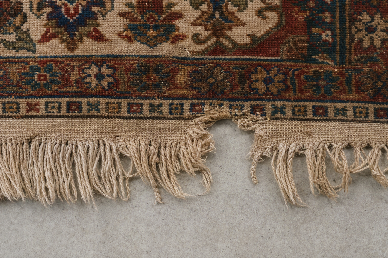 Close-up of a worn, partly missing rug fringe being assessed before repair