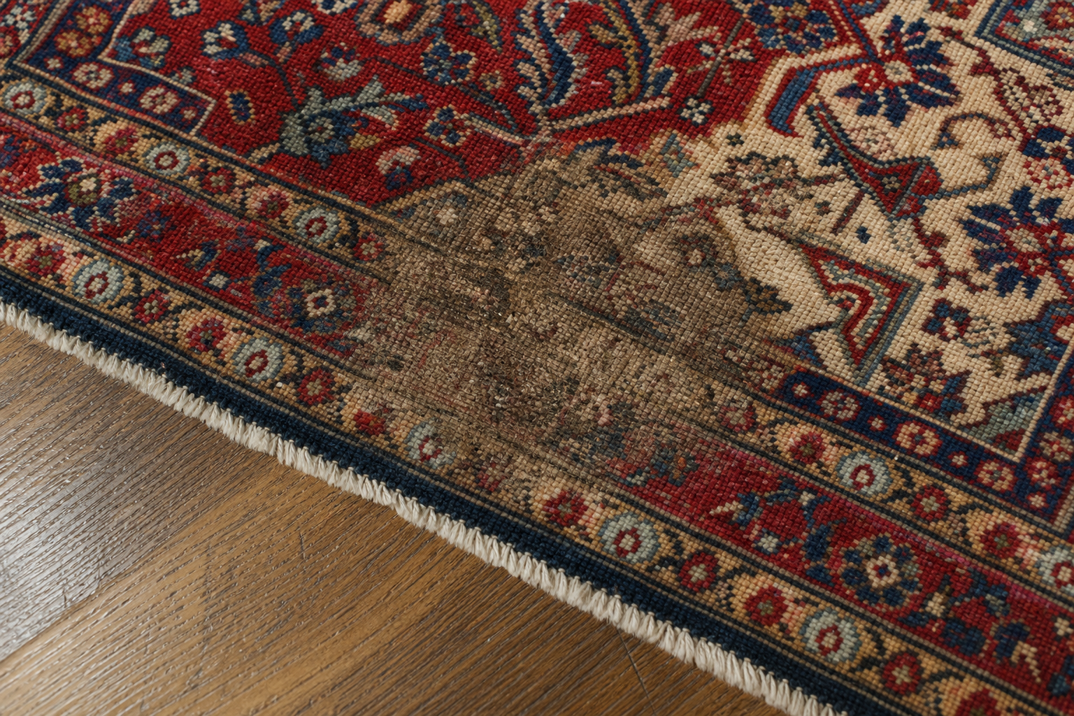 Close-up of a rug where a faded brown pet stain sits beside the still-vibrant original colors