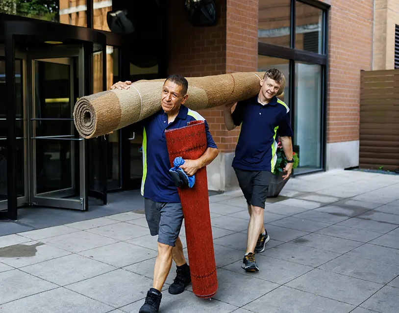 Two technicians carefully carrying a rolled hand-knotted oriental rug for cleaning